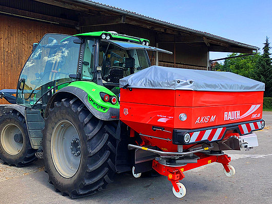 Ein Deutz Traktor mit einem Düngerstreuer von hinten.