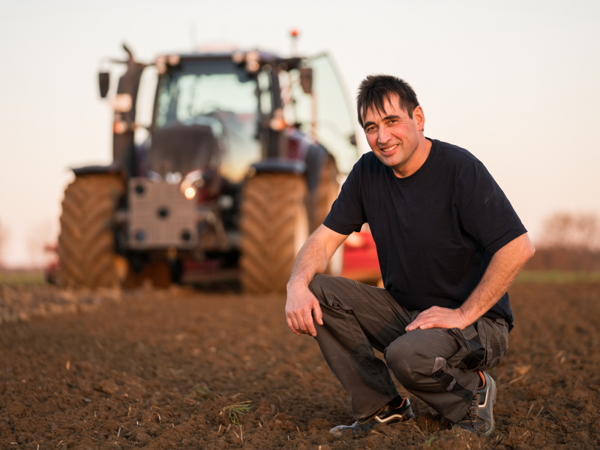 Landwirt Wilfried Veitengruber kniet auf einem Acker vor seinem Valtra Traktor im Hintergrund