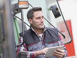 Mann steht mit Tablet vor Traktor.