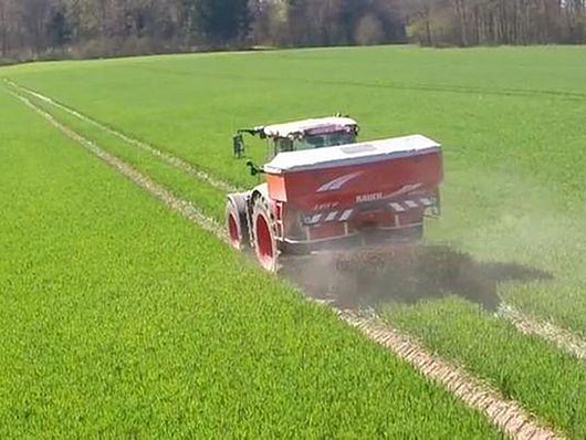 Traktor beim Dünger streuen auf einem Feld.