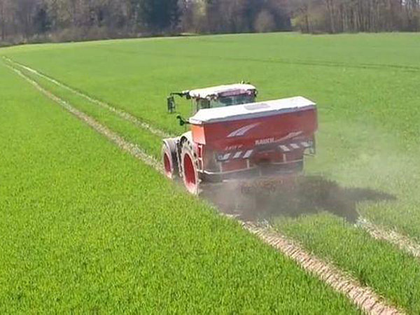 Traktor beim Dünger streuen auf einem Feld.
