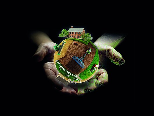 NEXT Farming Key Visual: Weltkugel symbolisiert Welt der Landwirte und schwebt über zwei Händen vor schwarzem Hintergrund