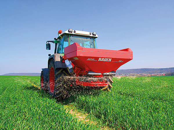 Fendt-Traktor streut in einem jungen Weizenfeld Dünger mit Rauch Düngerstreuer