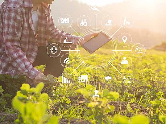 Mann kniet im Feld mit Tablet in der Hand und um das Tablet befinden sich Symbole wie WLAN, Traktor und viele mehr.