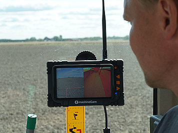 Monitor der MachineCam von Luda.Farm auf Traktor montiert und Mann schaut in Bildschirm.