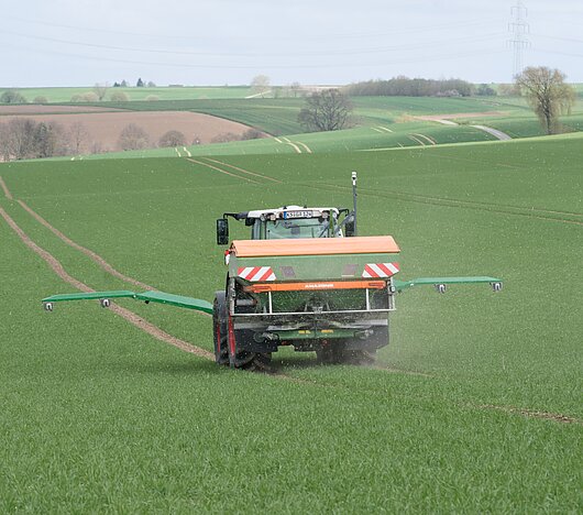 Fendt-Traktor mit Amazone Düngerstreuer und NEXT GreenSeeker fährt über ein Feld, fotografiert von hinten