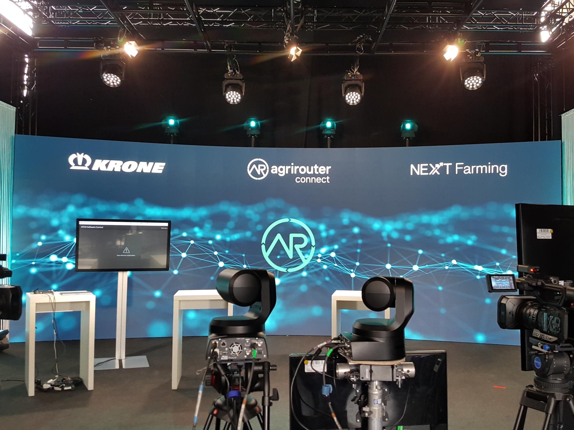 Banner des agrirouter connect Events mit Krone und NEXT Farming, im Vordergrund darauf gerichtete Kameras und Scheinwerfer
