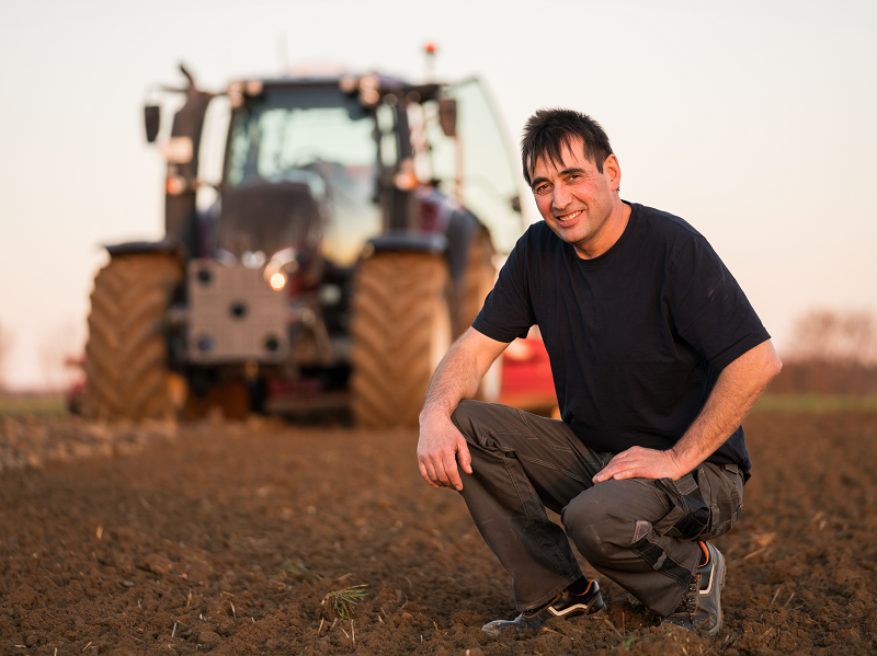 Landwirt Wilfried Veitengruber kniet auf einem Acker vor seinem Valtra Traktor im Hintergrund